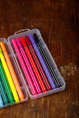 Multicolored marker or fine liner pens in plastic case on wooden table background. Art tools