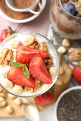 Delicious chocolate pudding with chia seeds, strawberries, yogurt and nuts in glass on white table, flat lay
