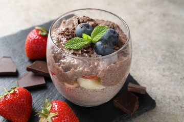 Delicious chocolate pudding with chia seeds, strawberries and blueberries in glass on light grey...