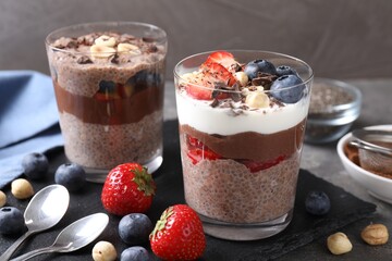 Delicious chocolate puddings with chia seeds, nuts and berries in glasses on grey table, closeup