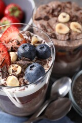 Delicious chocolate puddings with chia seeds, nuts and berries in glasses on table, closeup