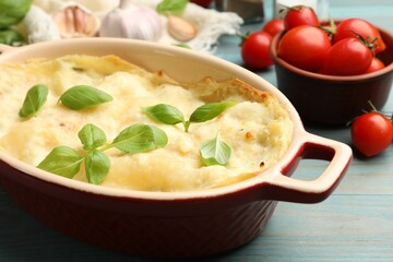 Tasty vegetarian lasagna and ingredients on light blue wooden table, closeup