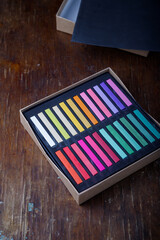 Box of professional multicolored dry pastel chalks or crayons sticks on wooden table background....