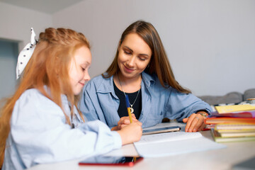 A young schoolgirl and her mother do their homework and write with a pen in a notebook
