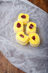 Turkish delight, yellow locum roll with jelly and coconut flakes on white paper, wooden background. Eastern sweets, oriental food. Traditional tasty dessert. Copy space. Top view