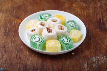 Turkish delight, green yellow and white locum roll with walnut on plate, wooden background. Eastern sweets, oriental food. Traditional tasty dessert