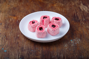 Turkish delight, pink and white locum roll with walnut and jelly on paper, wooden background. Eastern sweets, oriental food. Traditional tasty dessert