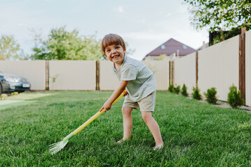 Happy boy playing in the garden, holding a rake and smiling brightly. The scene captures joy and...