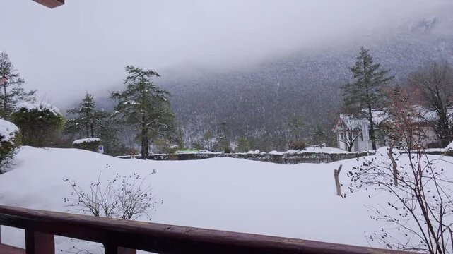 A misty snow-covered mountain viewed from a wooden balcony in Yunnan, China&mdash;featuring frosted trees, distant buildings, and quiet wintry ambiance in an alpine ethnic landscape.