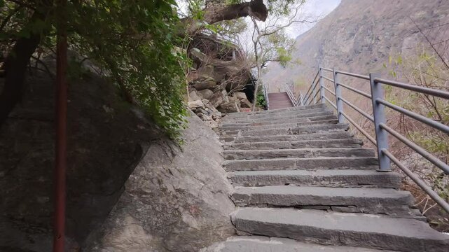 A set of stone stairs ascends through a rocky slope in Yunnan&rsquo;s highland terrain&mdash;featuring metal railings, rugged textures, and the scenic backdrop of distant mountains and sparse greenery.