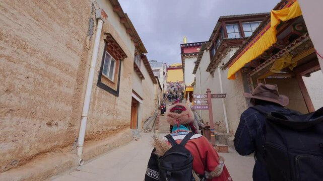 Two people walk toward the entrance of Songzanlin Monastery in Shangri-La, Yunnan&mdash;framed by traditional Tibetan architecture and banners, evoking the start of spiritual discovery and ethnic immersion.