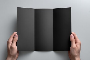 Hands hold open tri-fold black brochure