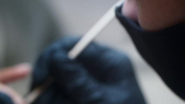 Professional female nail technician using wooden stick to gently push back cuticles on natural nails while wearing black gloves for hygiene and precision