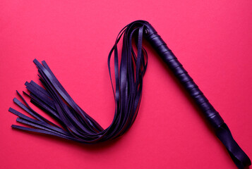 Leather black whip for sex games on a red background. BDSM toys for role-playing sex games.