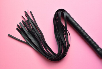Leather black whip for sex games on a pink background. BDSM toys for role-playing sex games.