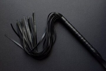 Leather black whip for sex games on dark gray background. BDSM toys for role-playing sex games. Dark photo