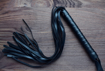 Leather black whip for sex games on a wooden background. BDSM toys for role-playing sex games. Dark...