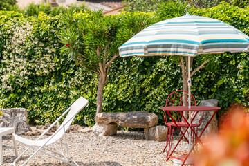 Coin détente au jardin avec parasol rayé et banc en pierre rustique