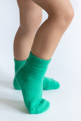 Legs of a 2 year old baby in warm green socks on a white background