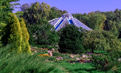 Beautiful botanical garden featuring a modern glass structure surrounded by lush greenery and colorful flowers