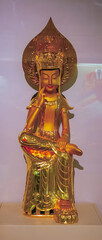 Beautiful golden statue of a Buddhist figure displayed in a museum gallery surrounded by soft lighting