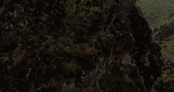 A drone flies around a young athletic female climber hanging on one arm on a belay on a steep cliff