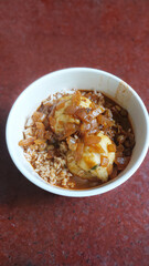 A bowl of potato dumplings with rice topped with caramelized onions on a red surface, a simple homecooked dish