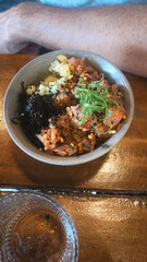 A poke bowl with tuna, seaweed, chives, and sesame seeds on a wooden table, an authentic...