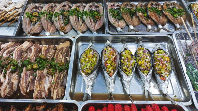 Marinated bangus or milkfish and marinated pork with vegetables displayed in trays ready for grilling in a street food stall showing a glimpse of the Philippines local cuisine and culture