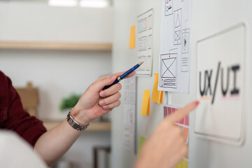 UX and UI Design. Focused hands pointing at wireframes and design elements on a wall.
