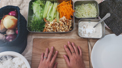 Hands positioned on a wooden board surrounded by fresh ingredients for making kimbap or gimbap...