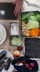 Hands putting rice on a sheet of seaweed or nori in the process of making kimbap or gimbap, a traditional local South Korean dish