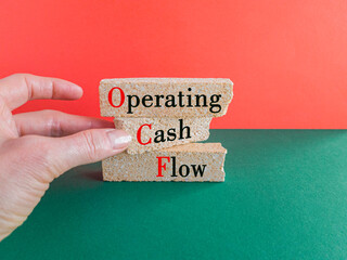 Concept words OCF-operating cash flow on brick blocks. Beautiful green table, red background....