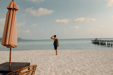 A lone person walking on the sandy beach with an umbrella and wicker chair on the foreground and the ocean in the background. Koh Rong Sanloem, Sihanoukville, Cambodia