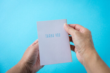 Holding a Thank you card. Against light blue background.