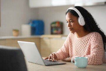 Fototapeta premium Black woman using laptop and headphone in a kitchen