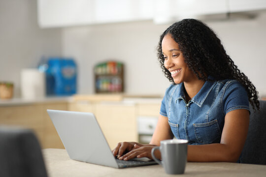 Happy black woman typing on laptop in a kitchen