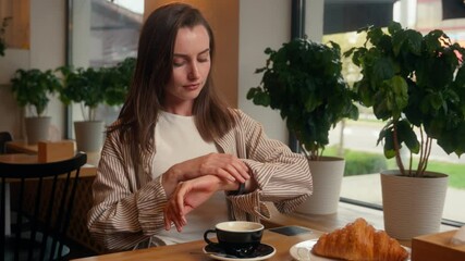 Caucasian woman visitor in cafe checking time with wristwatch late business meeting looking in window waiting date lonely girl female at cafeteria table worry wait impatient lateness upset frustrated