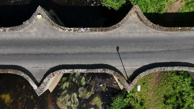 Clady Bridge, County Tyrone, Northern Ireland, June 2023. Drone top down tracking pan left over arched bridge with unique scalloped walls at midday.