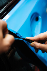 Precision PPF wrapping and detailing on car panel using sharp blade to trim wrap with accuracy. Car detailing involves precise vinyl cutting techniques. Precision cutting of PPF wrap on car body.