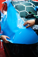 Applying PPF wrap on car during full detailing. Bold blue vinyl wrap installing in detailing...