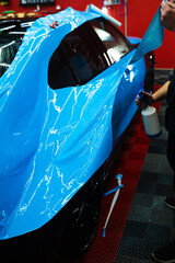 Detailing experts use hydration spray for controlled application of blue PPF film. Detailer uses...