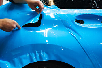 Detailing technician trims blue PPF on a car panel for perfect contour fit. Cutting blue PPF with...