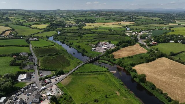 Clady Bridge, County Tyrone, Northern Ireland, June 2023. Drone panoramic high angle orbit clockwise and tilt up across pasture fields with arched bridge at center.