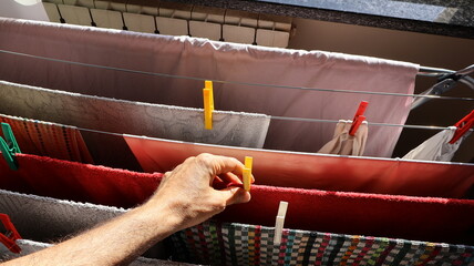 Clothesline close up drying clothes indoors and man's hand holds a clothespin.