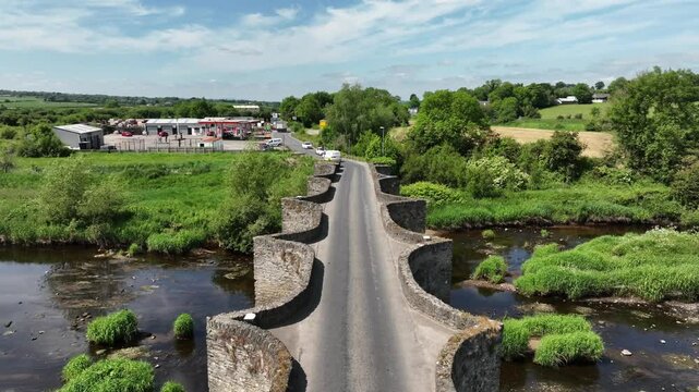 Clady Bridge, County Tyrone, Northern Ireland, June 2023. Drone approach tracking following car zooming away into distance as people wait on the other side to cross the River Finn.