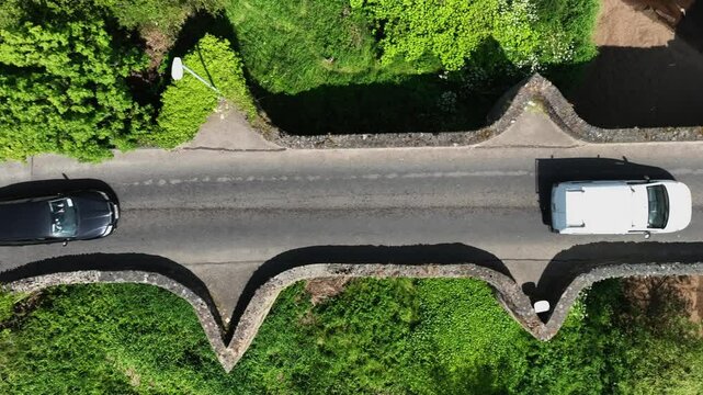 Clady Bridge, County Tyrone, Northern Ireland, June 2023. Drone tracking right follows cars crossing arched bridge over River Finn.