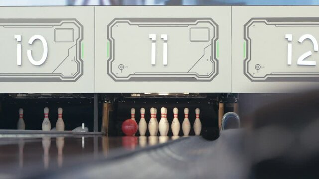 Asian person in casual outfit rolls a bowling ball smoothly on the lane toward the pins, captured indoors with clear background, showing focus, motion, and game preparation