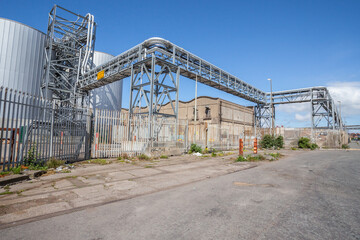 Fototapeta premium Weathered industrial tanks and scaffolding stand against a cloudy sky. An active site displaying signs of age, ongoing maintenance, and sustained operational use