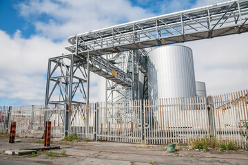 Weathered industrial tanks and scaffolding stand against a cloudy sky. An active site displaying...